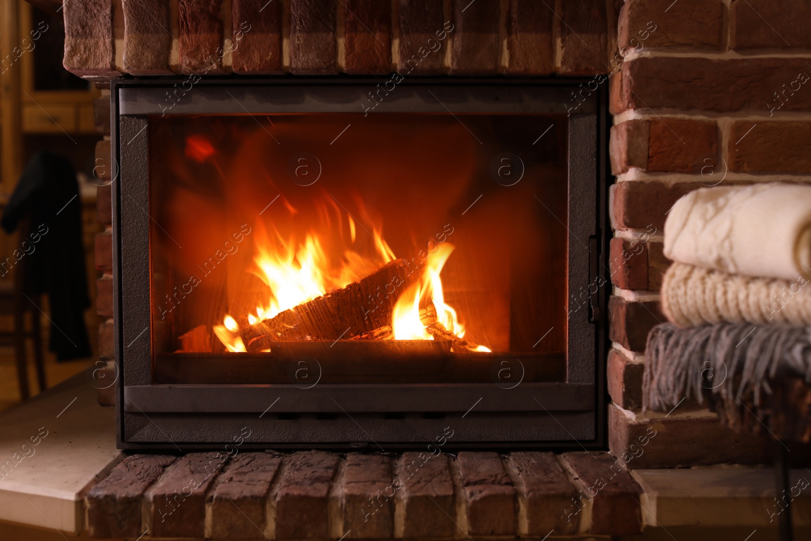 Photo of Stack of knitwear near fireplace with burning wood indoors. Winter vacation