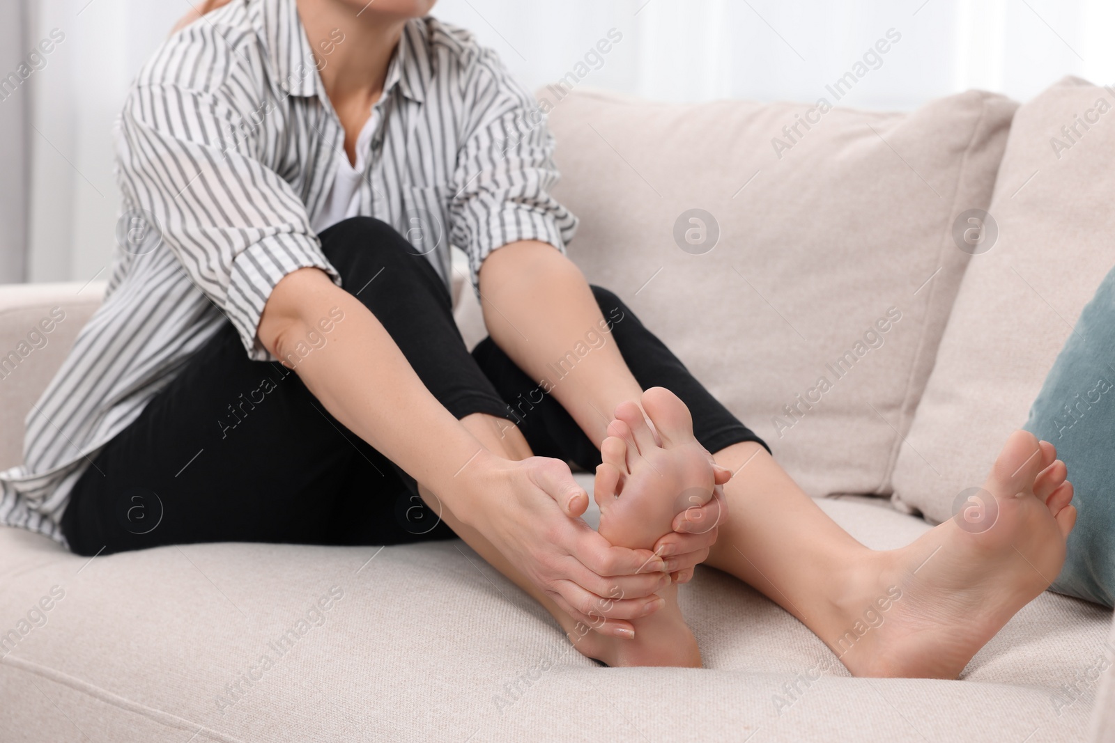 Photo of Woman suffering from foot pain on sofa indoors, closeup. Arthritis symptoms