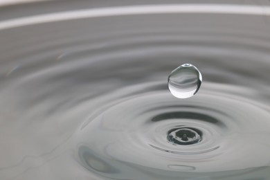 Photo of Drop falling into clear water on light grey background, closeup. Space for text