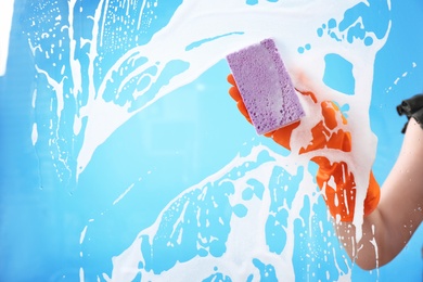 Photo of Woman cleaning glass with sponge against color background