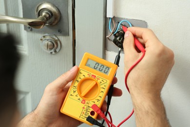 Professional electrician with tester checking light switch voltage indoors, closeup