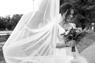 Photo of Young bride with bouquet in long veil outdoors, black and white effect