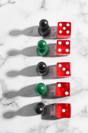 Photo of Red dices and game pieces on white marble table, flat lay