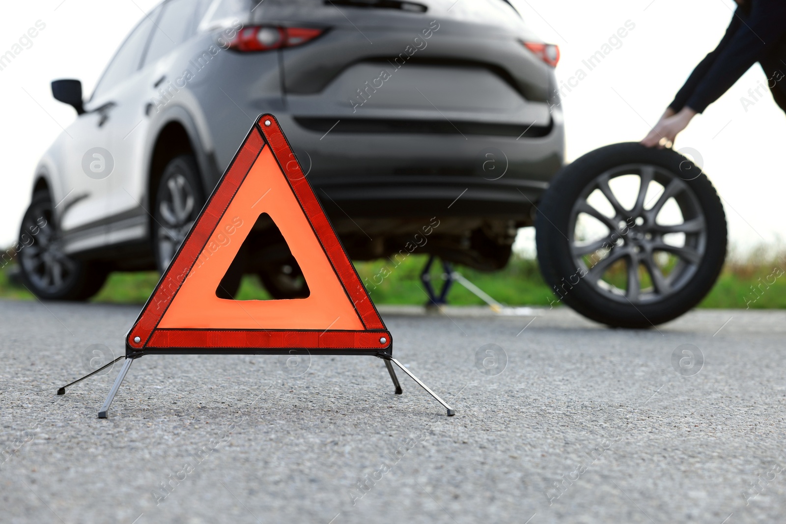 Photo of Man changing car tire near road, focus on emergency warning triangle