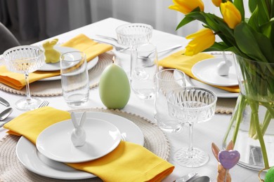 Photo of Festive table setting with glasses, burning candle and vase of tulips. Easter celebration