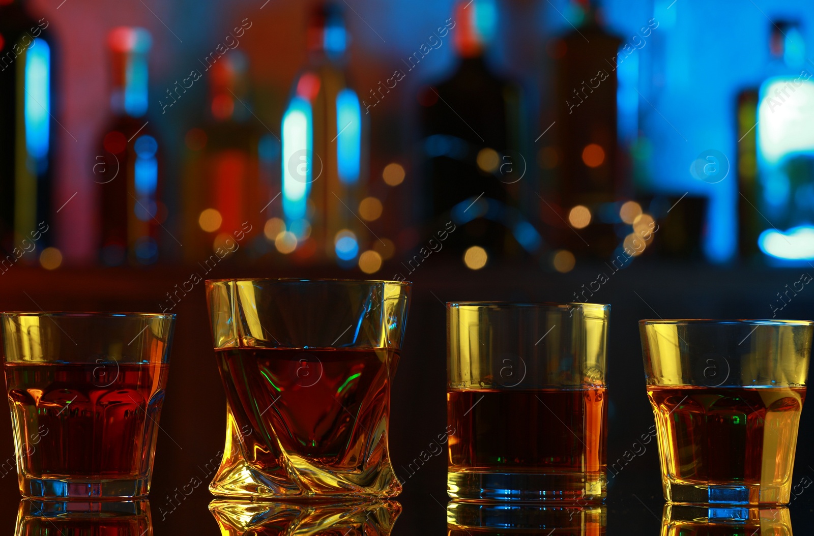 Photo of Different liqueurs in glasses on mirror table in bar, closeup