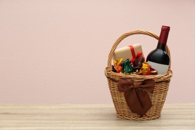 Wicker gift basket with food and wine on wooden table. Space for text