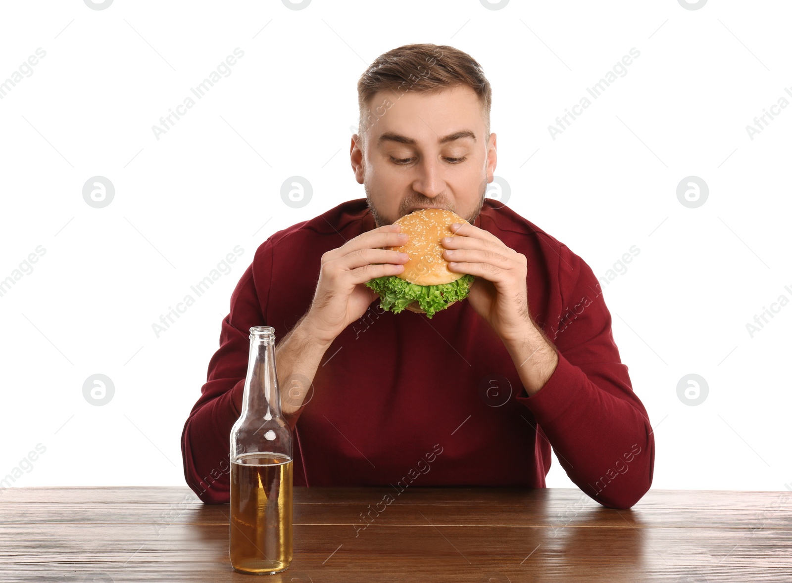 Photo of Young man with beer eating tasty burger at table on white background