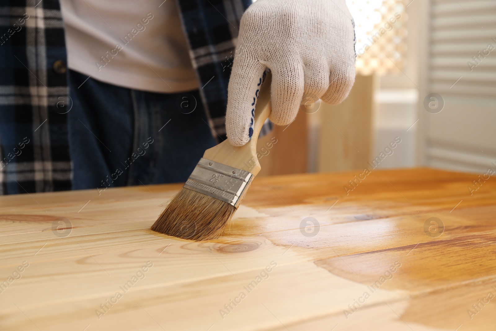 Photo of Man with brush applying wood stain onto wooden surface indoors, closeup