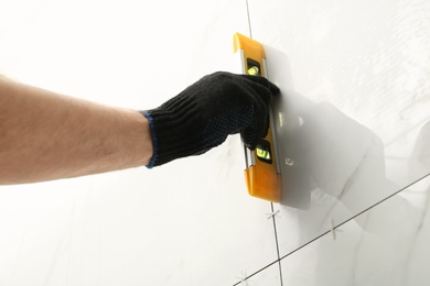 Photo of Man checking proper ceramic tile installation with level on wall, closeup. Building and renovation works