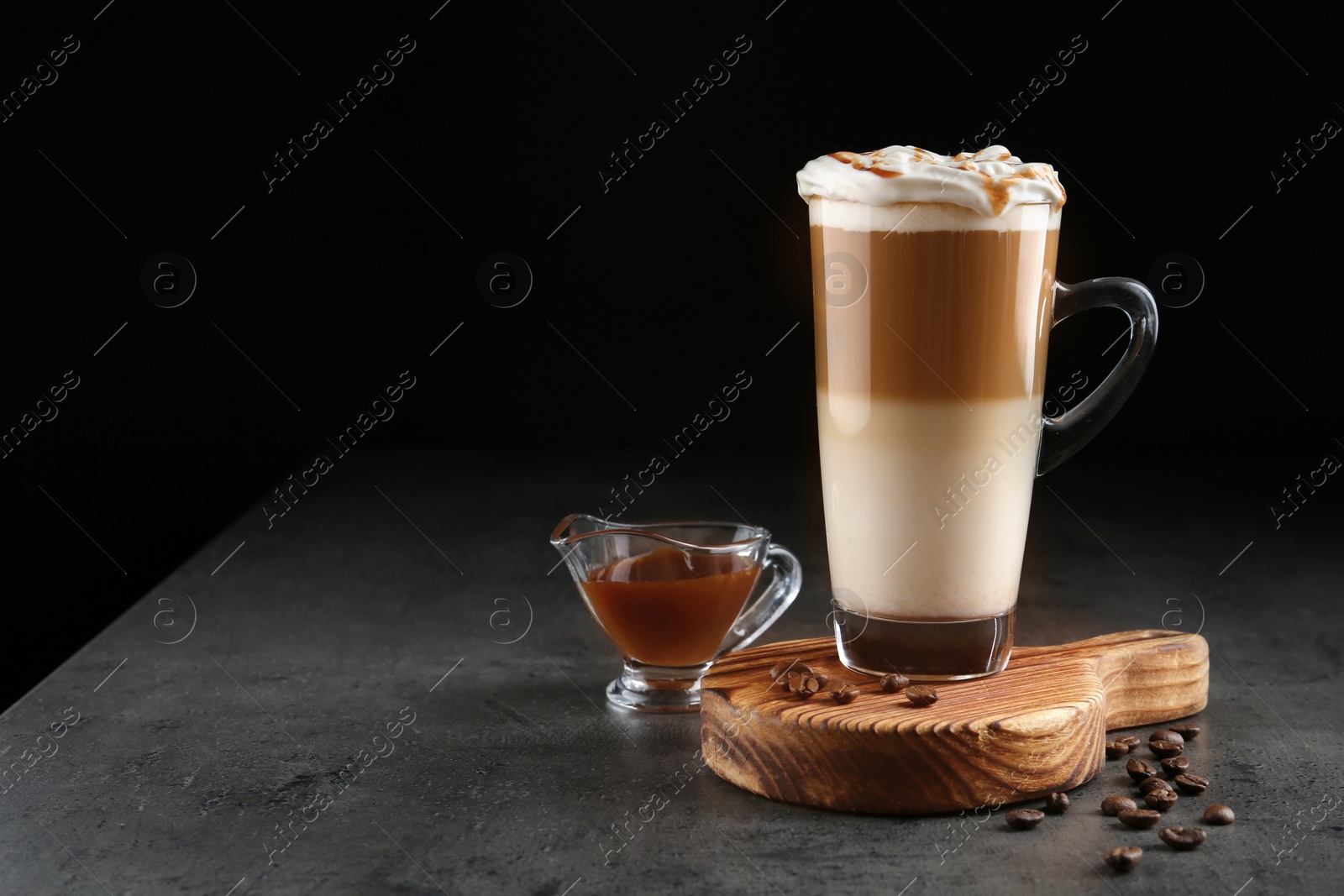 Photo of Glass cup of caramel macchiato and gravy boat with syrup on table, space for text