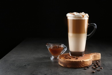 Glass cup of caramel macchiato and gravy boat with syrup on table, space for text