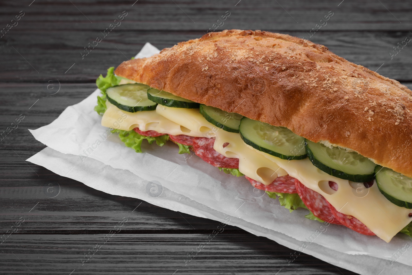 Photo of Delicious sandwich with cucumber, cheese, salami and lettuce leaves on wooden table, closeup