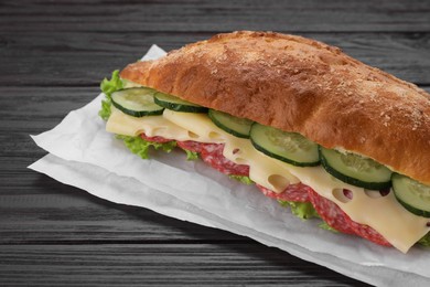 Photo of Delicious sandwich with cucumber, cheese, salami and lettuce leaves on wooden table, closeup