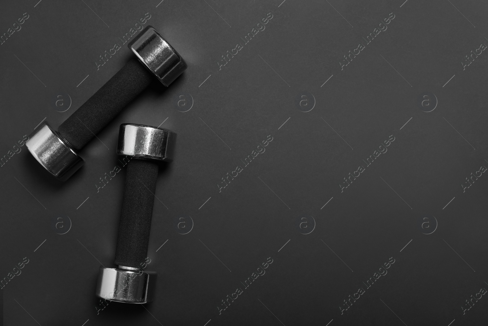 Photo of Dumbbells on black background, flat lay. Space for text