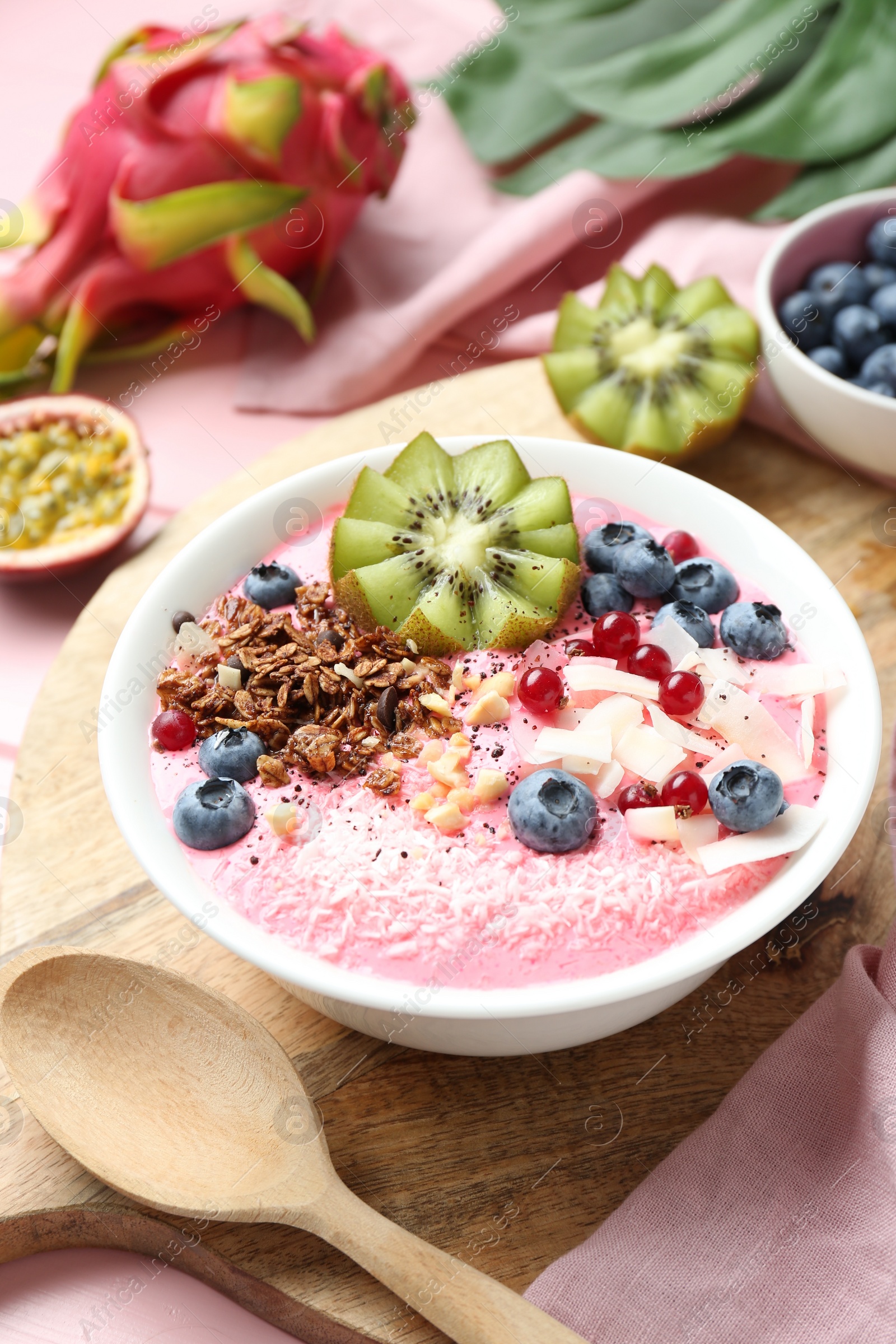 Photo of Tasty smoothie bowl with fresh kiwi fruit, berries and granola on pink table