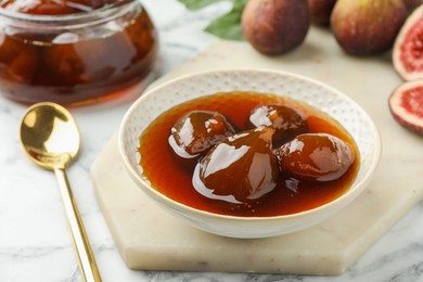 Photo of Bowl of tasty sweet fig jam on white marble table