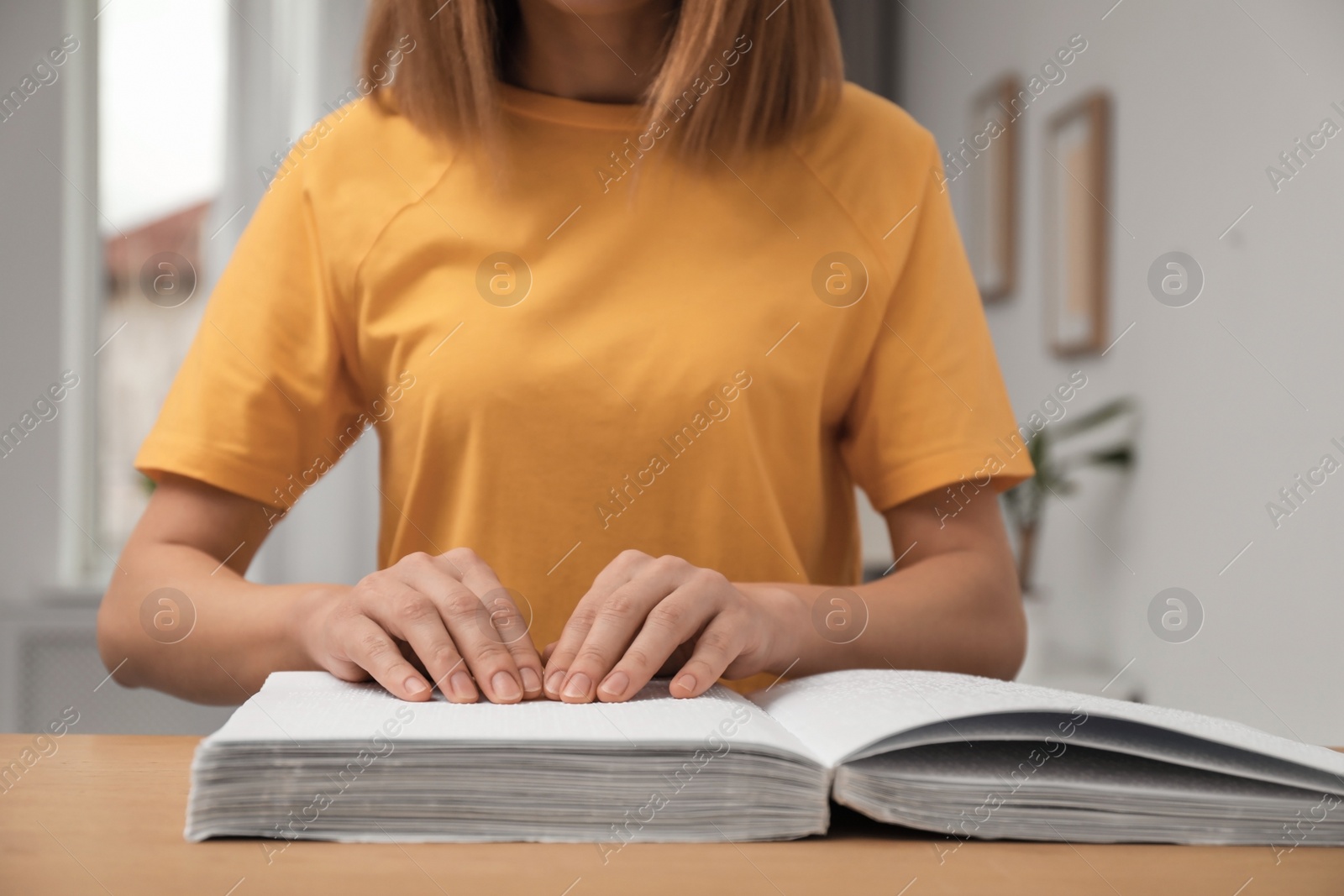 Photo of Blind woman reading book written in Braille at table, closeup