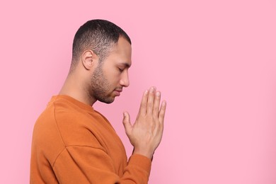 Photo of African American man with clasped hands praying to God on pink background. Space for text