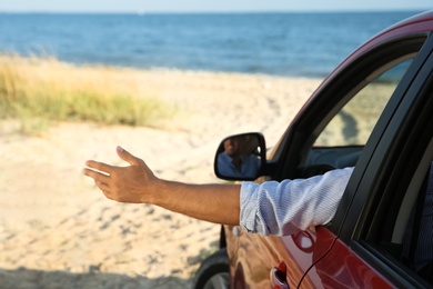 Man waving from car window on beach, closeup. Summer trip
