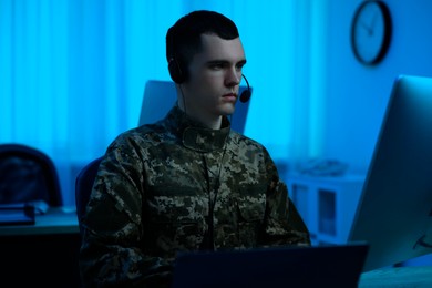Image of Military service. Soldier in headphones working at table in office at night