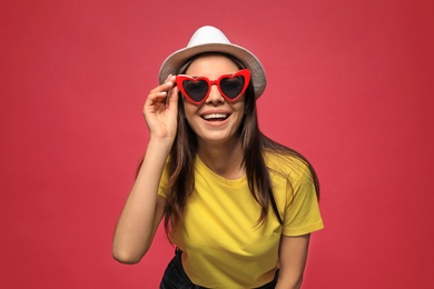 Portrait of beautiful young woman with heart shaped sunglasses on color background