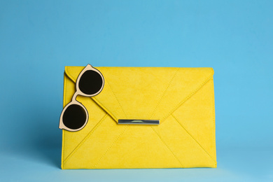 Stylish woman's bag and sunglasses on light blue background