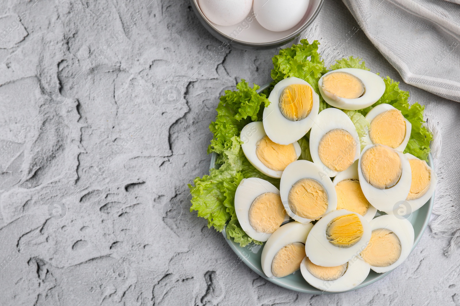Photo of Fresh hard boiled eggs and lettuce on light grey textured table, top view. Space for text
