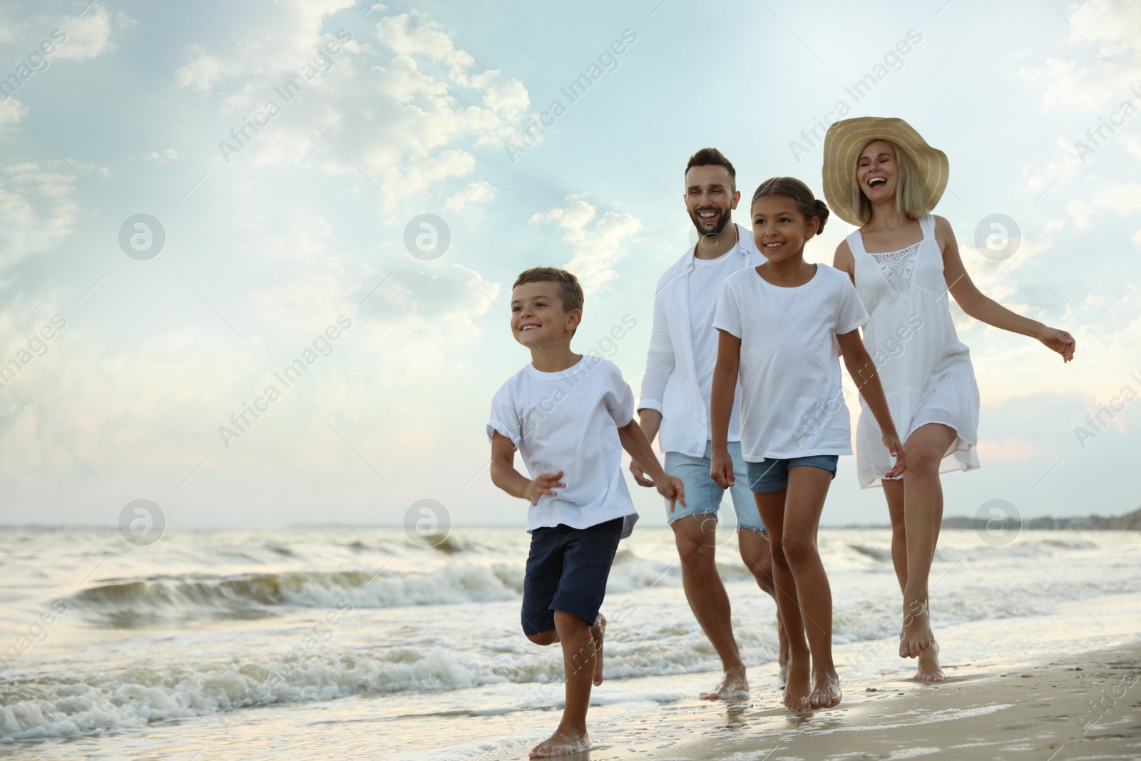 Photo of Happy family walking on sandy beach near sea at sunset