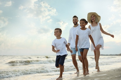 Photo of Happy family walking on sandy beach near sea at sunset