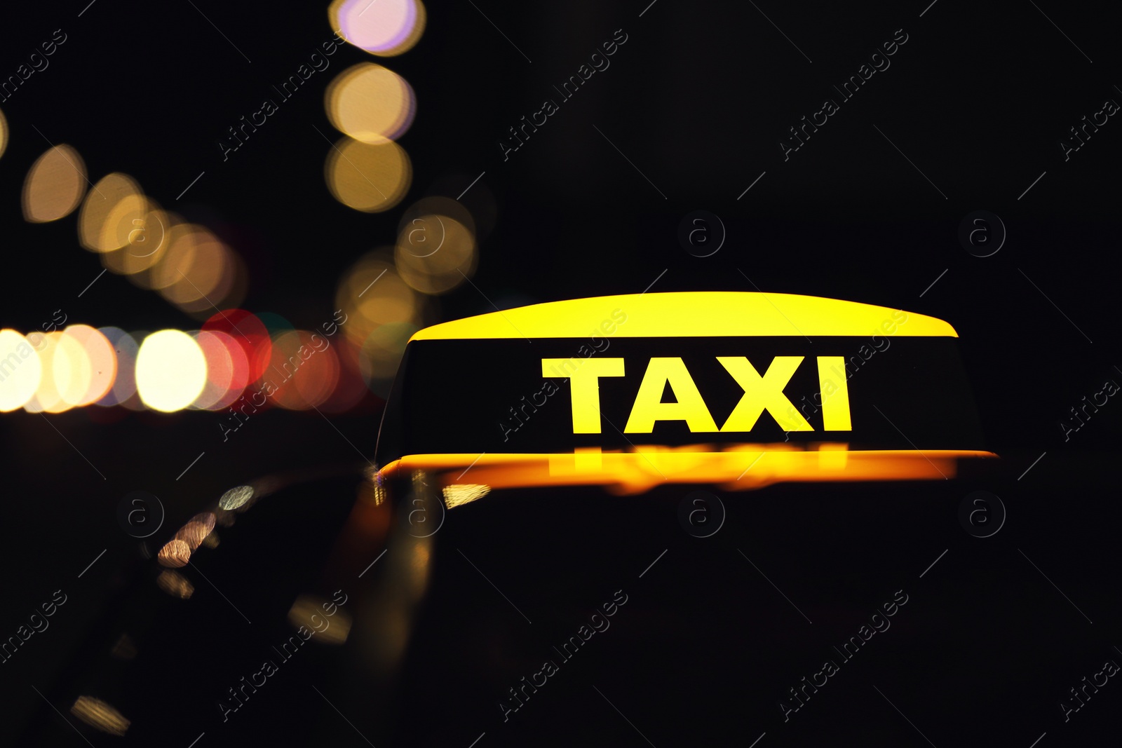 Photo of Taxi car with yellow roof sign on city street at night, closeup