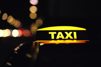 Taxi car with yellow roof sign on city street at night, closeup