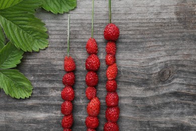 Photo of Grass stems with wild strawberries and leaves on wooden table, flat lay
