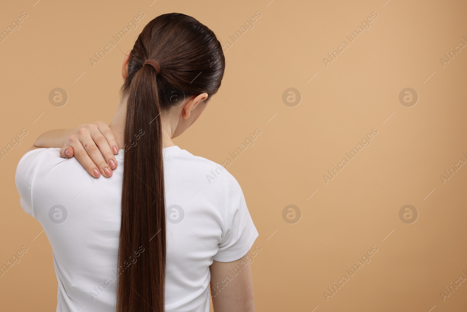 Photo of Woman touching her neck on beige background, back view. Space for text