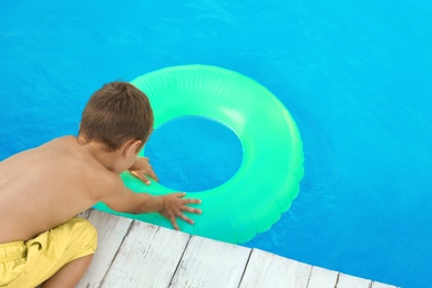 Photo of Little child reaching for inflatable ring in outdoor swimming pool. Dangerous situation