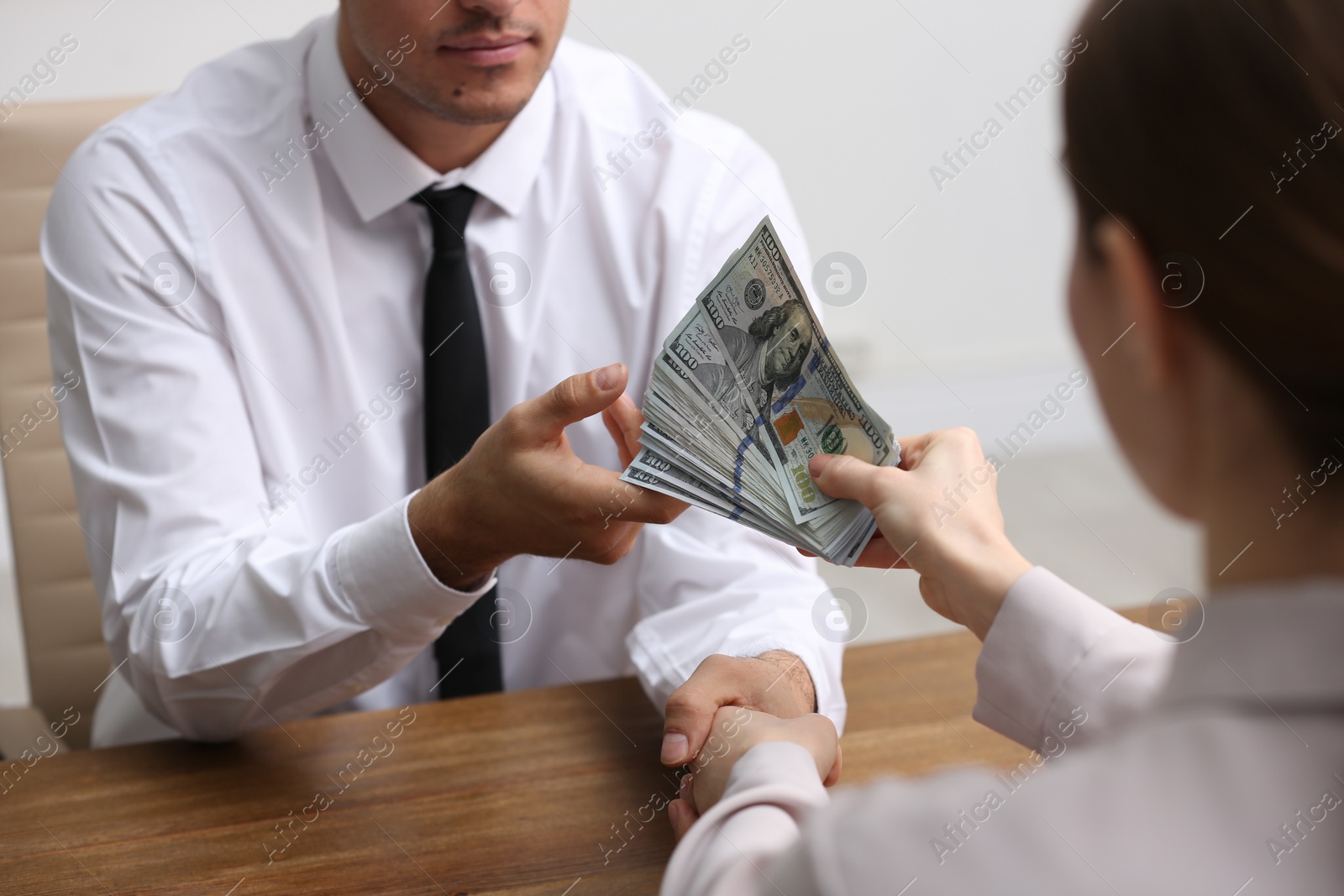 Photo of Woman shaking hands with man and offering bribe at table indoors, closeup