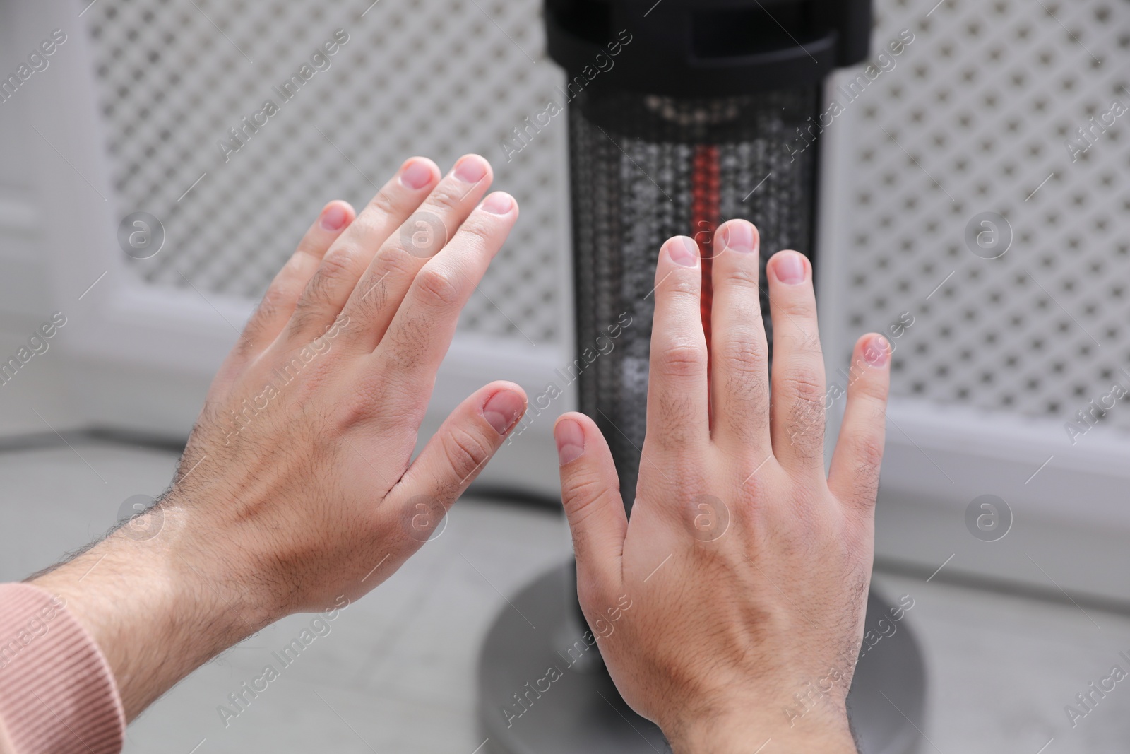 Photo of Man warming hands near modern heater indoors, closeup