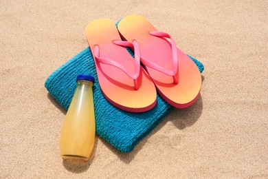 Photo of Stylish sunglasses, flip flops, towel and bottle of refreshing drink on sand
