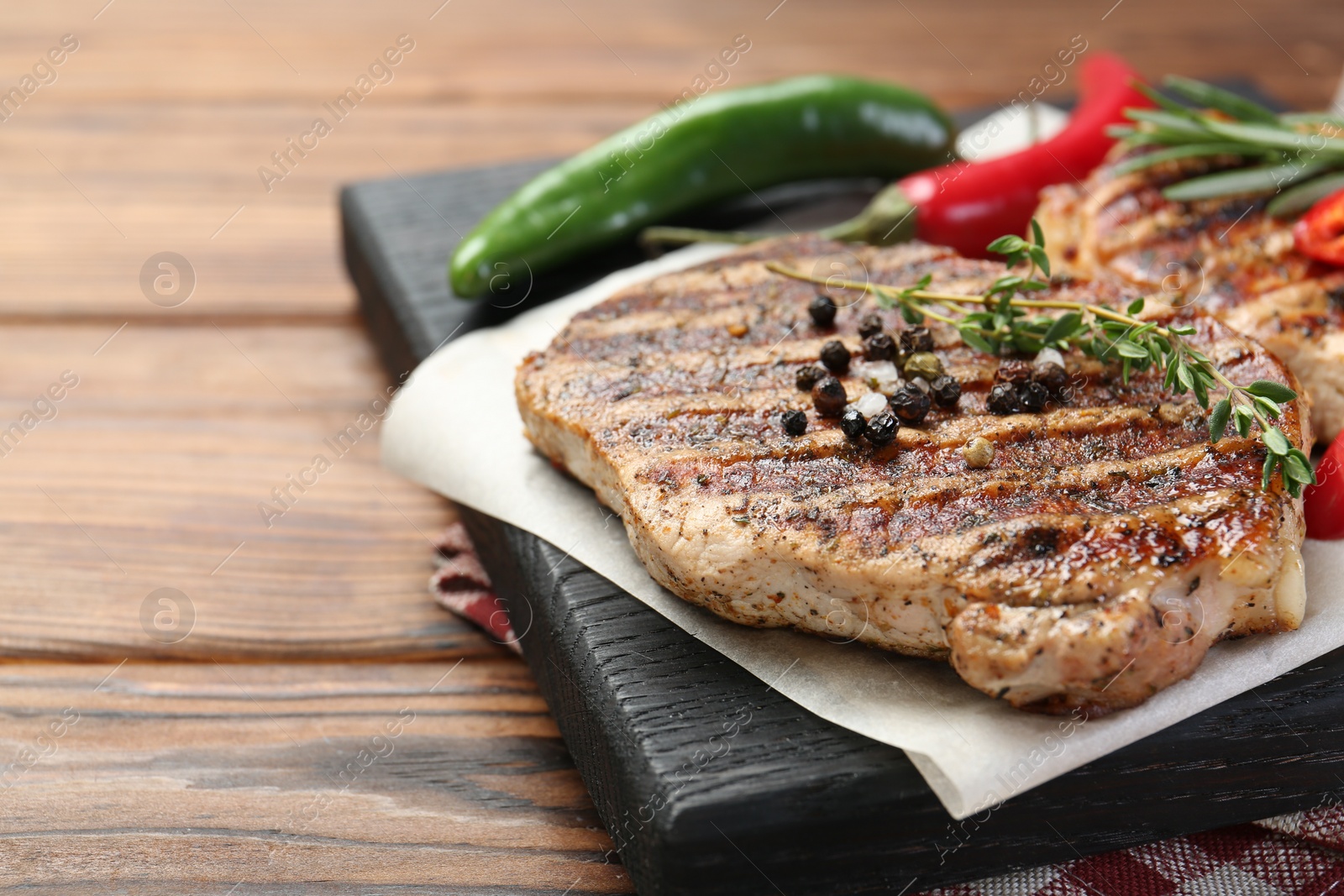 Photo of Delicious grilled pork steaks with spices on wooden table, closeup. Space for text
