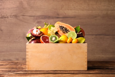 Photo of Different tropical fruits in box on wooden table
