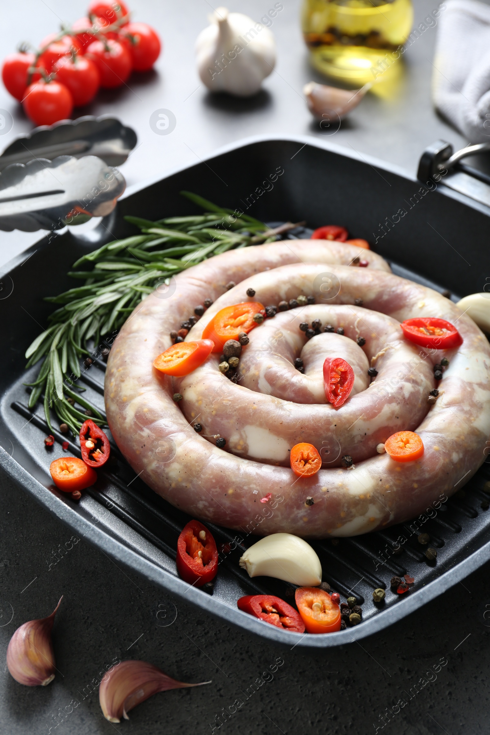 Photo of Pan with raw homemade sausage, chili pepper, garlic and rosemary on grey table, closeup