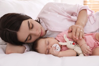 Photo of Young mother resting near her sleeping baby on bed