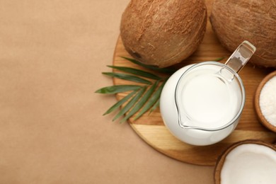 Glass jug of delicious vegan milk, coconuts and leaf on brown background, flat lay. Space for text