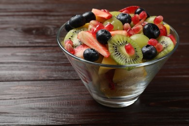 Photo of Tasty fruit salad in bowl on wooden table, closeup. Space for text