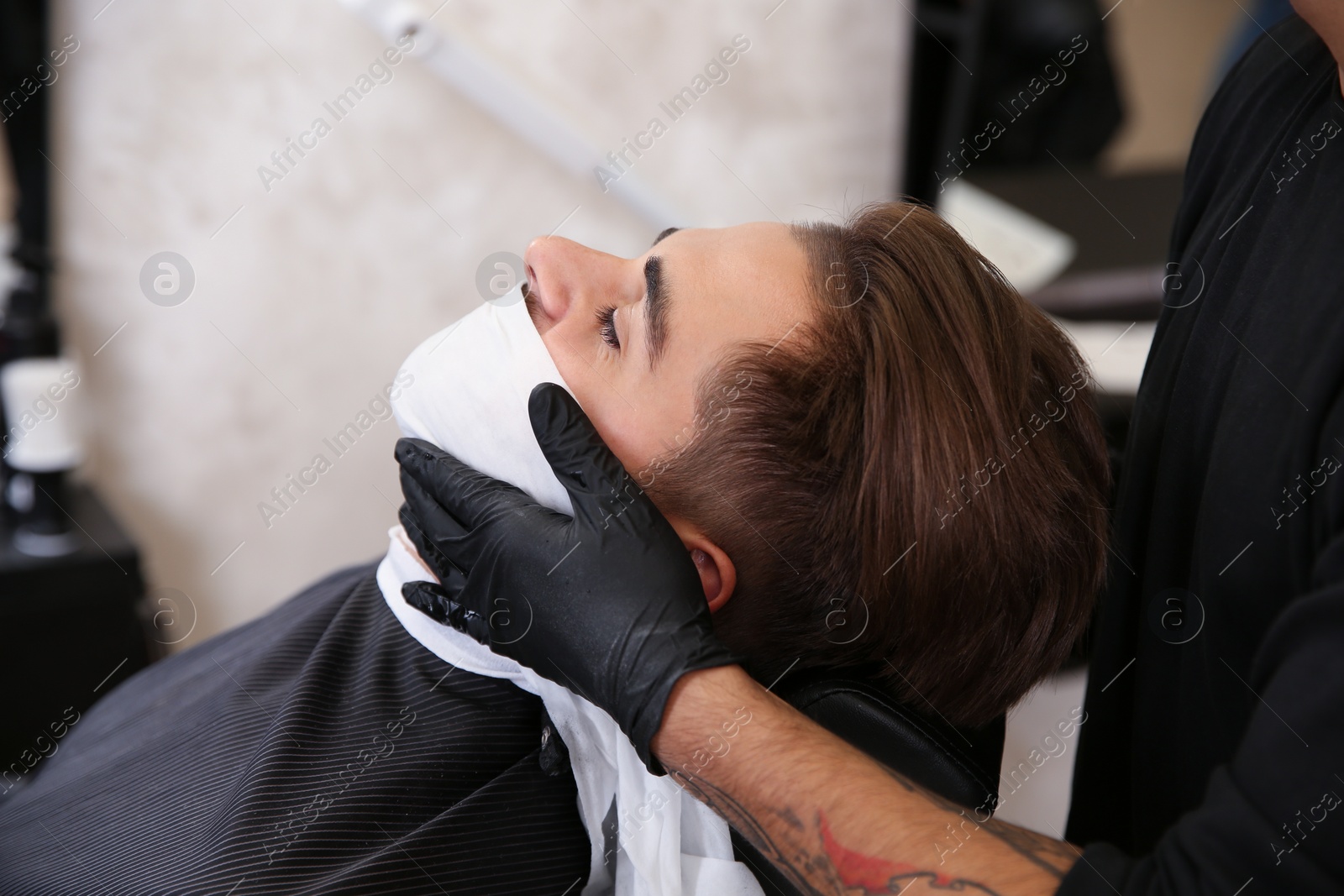 Photo of Professional hairdresser using cold towel to calm client's skin after shaving in barbershop