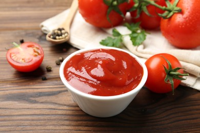 Photo of Delicious ketchup in bowl and tomatoes on wooden table, closeup