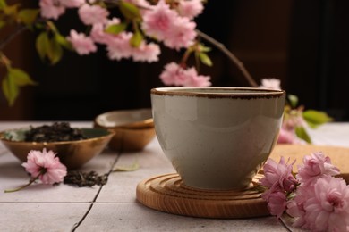 Photo of Traditional ceremony. Cupbrewed tea and sakura flowers on tiled table, closeup
