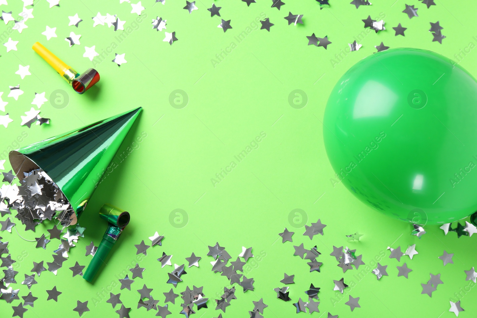 Photo of Frame made of party hat and other bright decor on light green background, flat lay