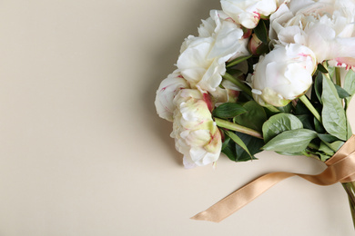 Photo of Bouquet of beautiful peonies with ribbon on beige background, flat lay. Space for text