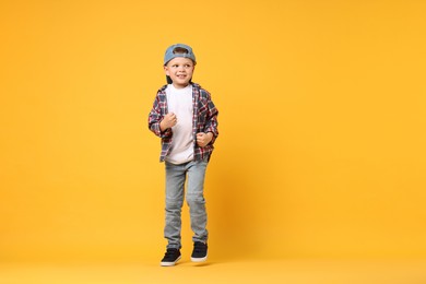 Photo of Happy little boy dancing on yellow background. Space for text